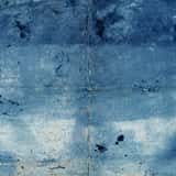 Dark blue stained grunge paper texture resembling a vintage cyanotype or watercolor wash, featuring heavy creases and dark ink spots.