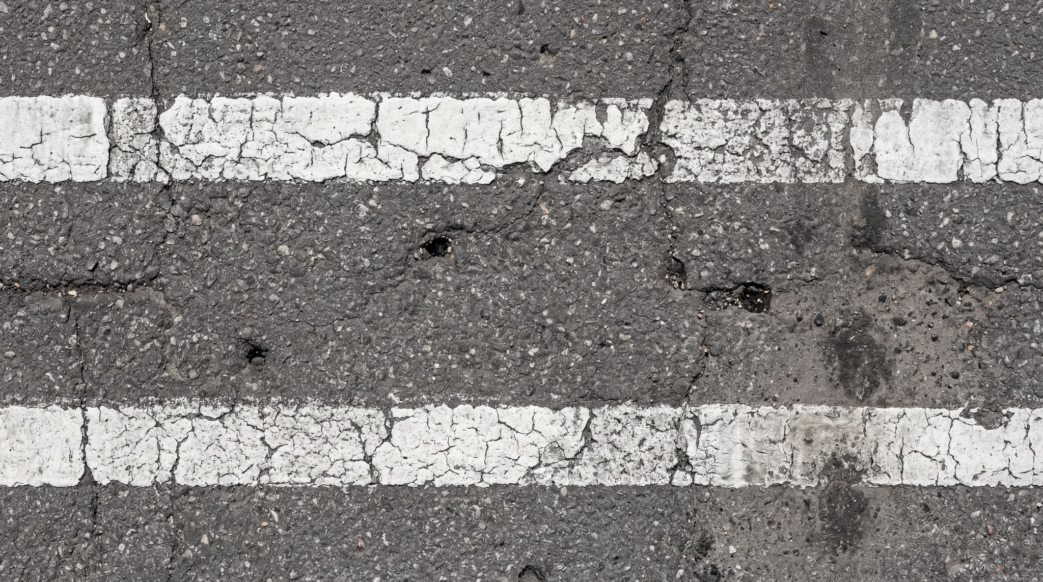 Close-up of a damaged asphalt road surface with two parallel, worn white road markings.