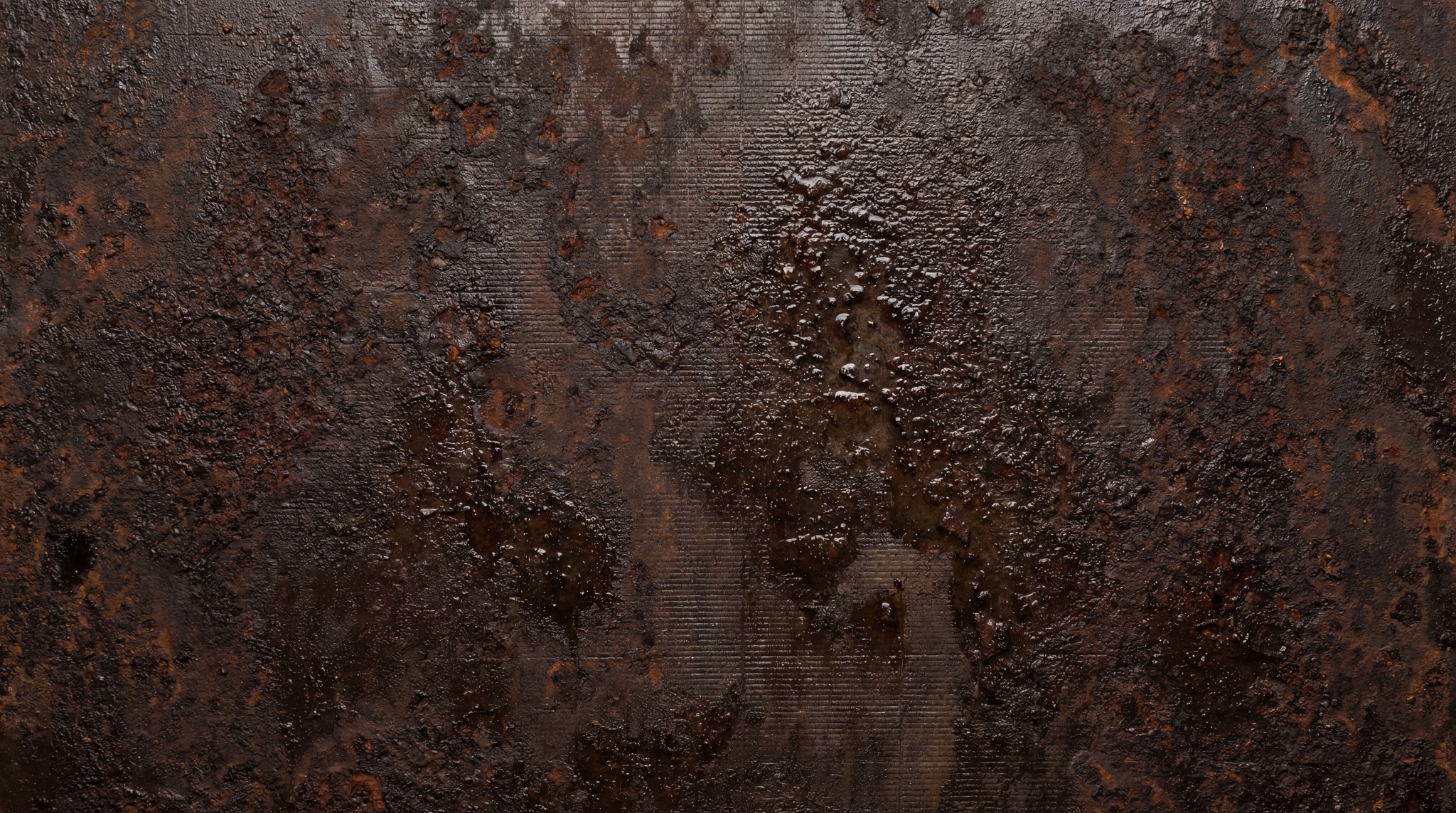Dark, heavily corroded metal surface with deep pitting and a bubbling, wet appearance.