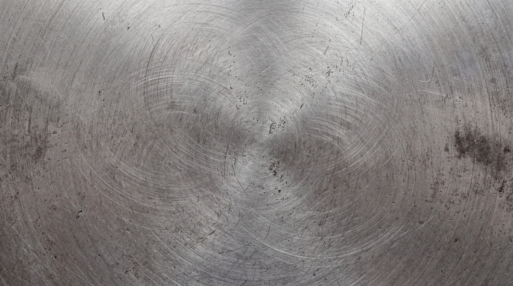 A close-up of a circular brushed steel surface with heavy rotational scratches and industrial wear.