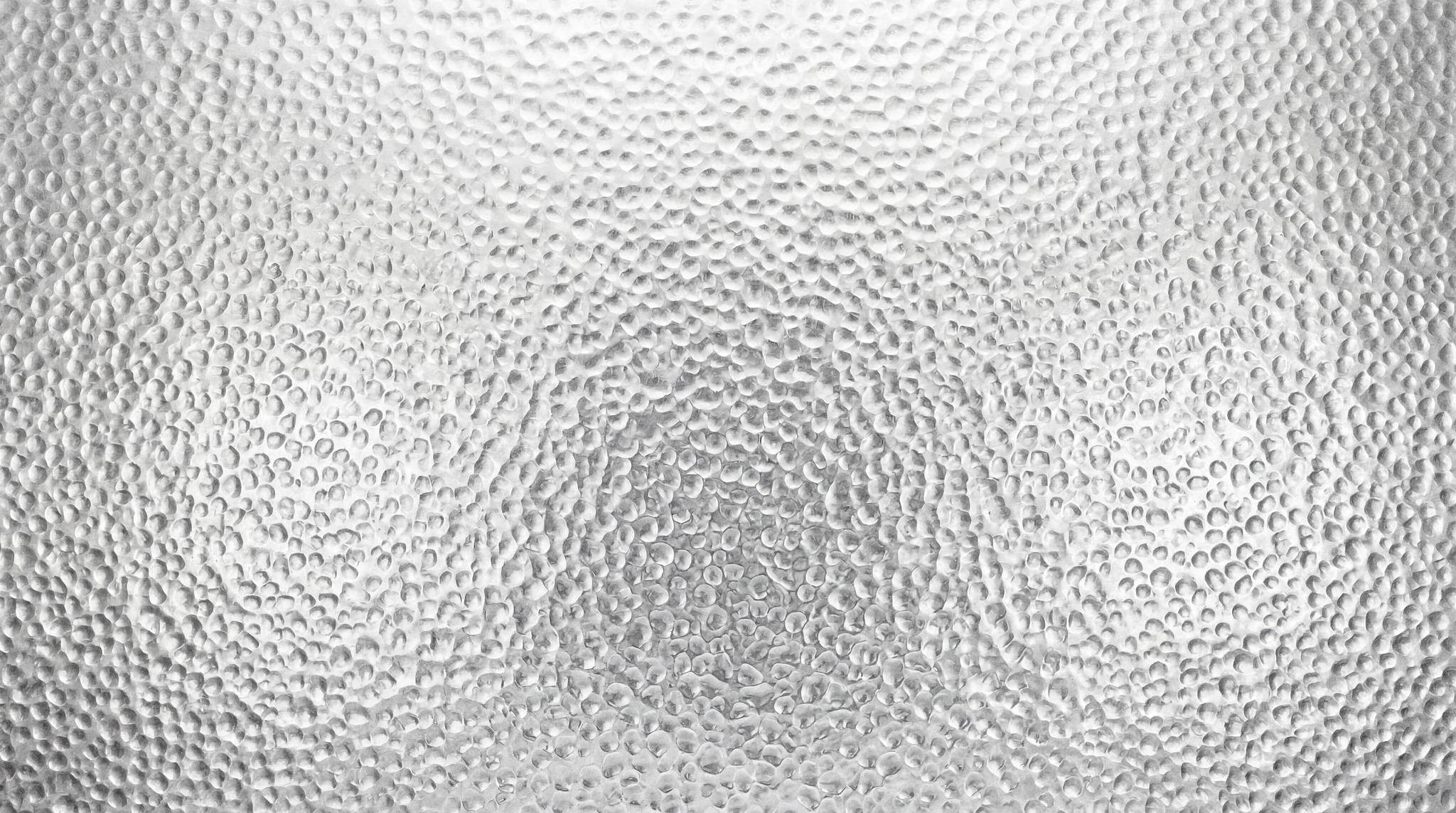 Close-up view of a high-resolution metallic surface featuring a repetitive hammered, dimpled texture pattern in a uniform silver-grey finish.