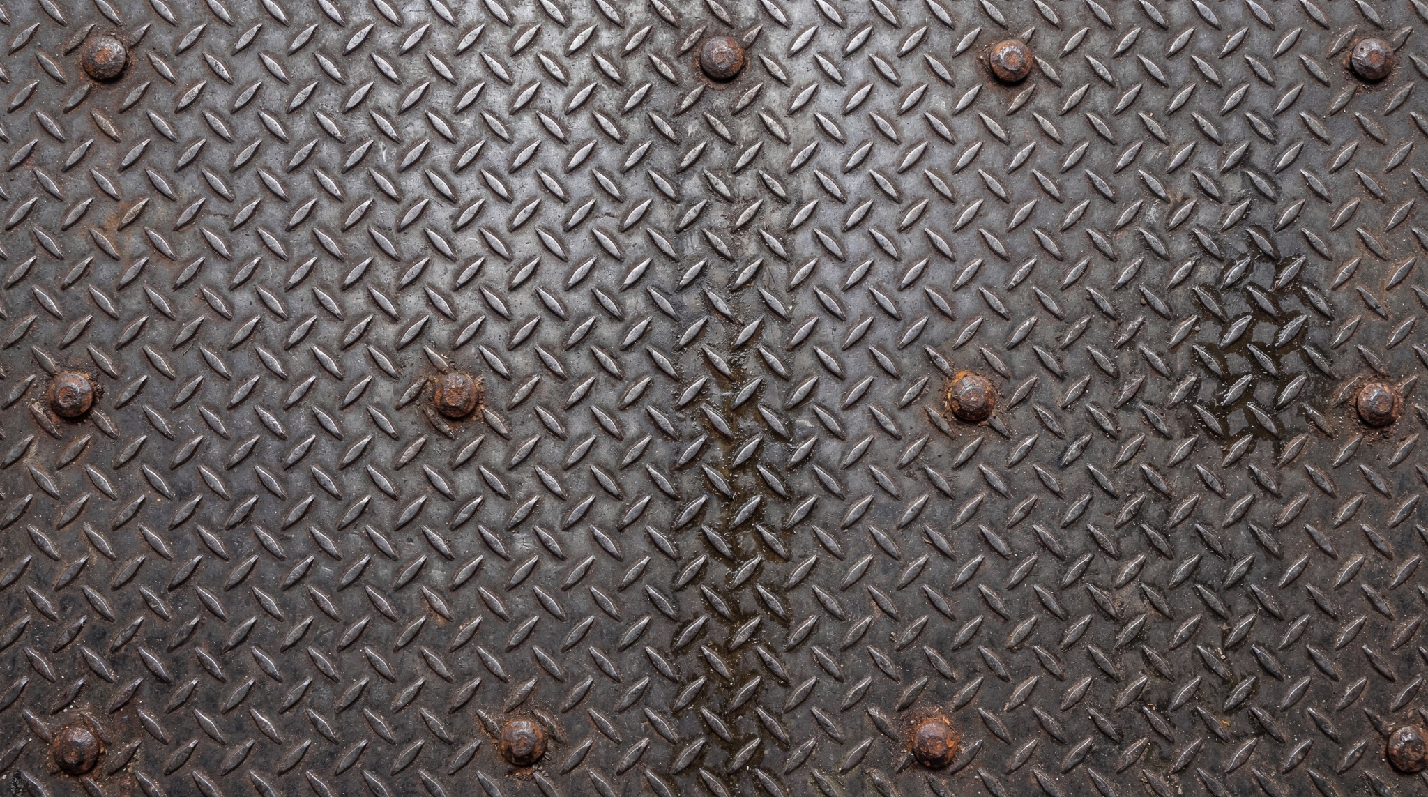 A close-up of a dark industrial diamond plate steel sheet with visible bolt heads.