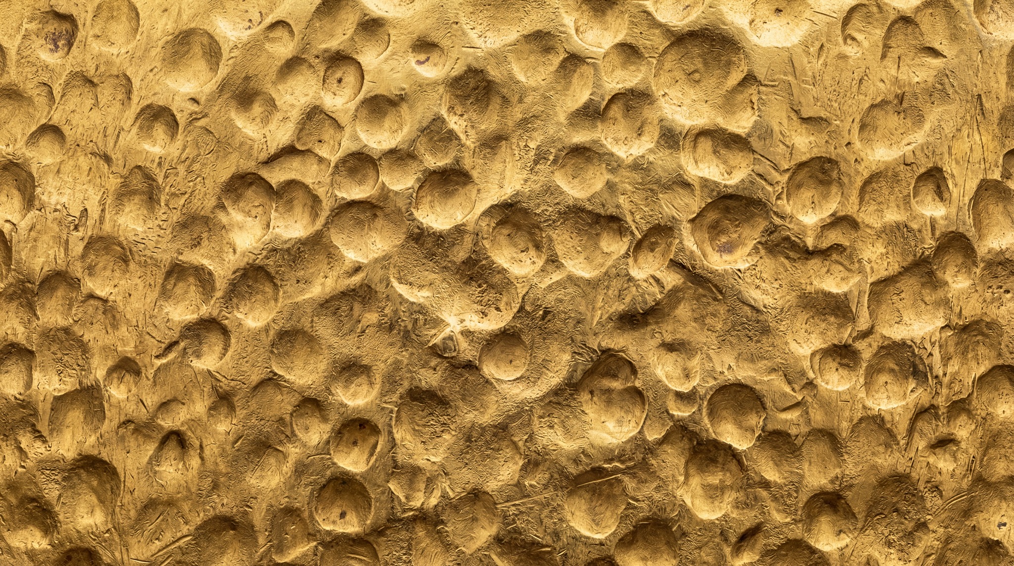Close-up view of a golden surface with numerous irregular, circular indentations, resembling hammered or molded metal.