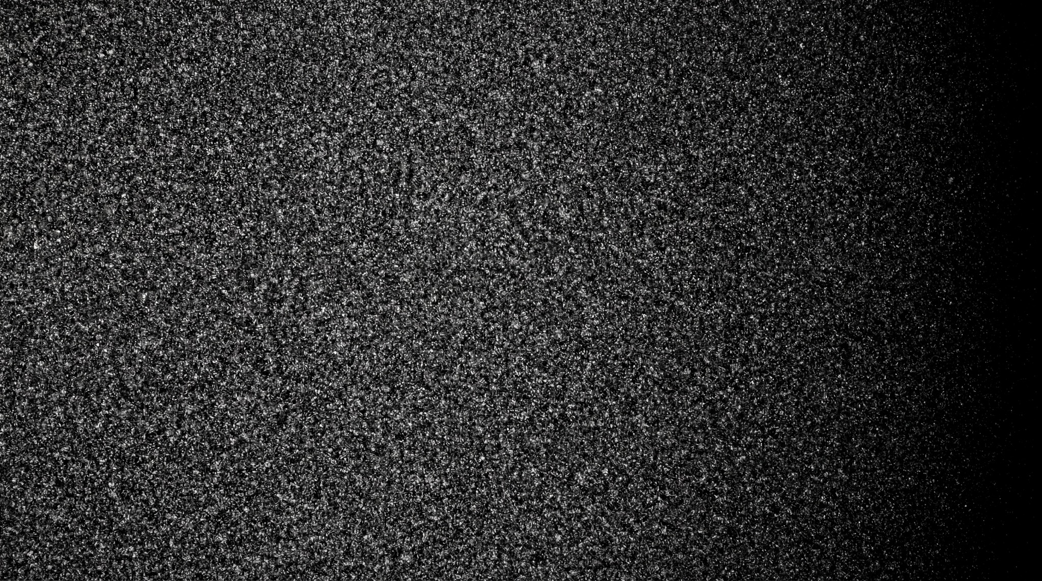 A dense, monochromatic film grain texture with subtle light falloff on the right.