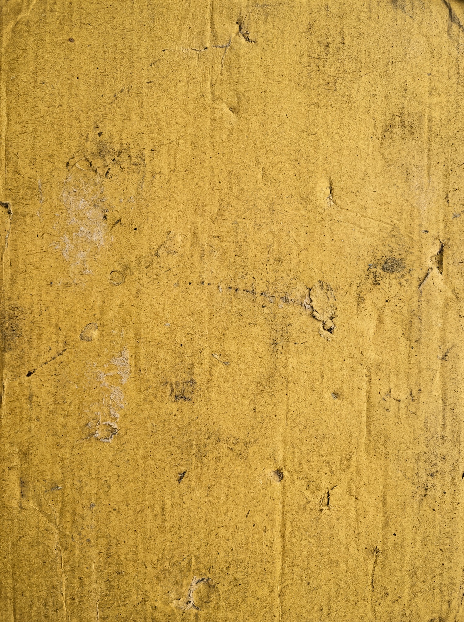 Close-up of a yellow painted cardboard surface with visible texture, scratches, and dark smudges.