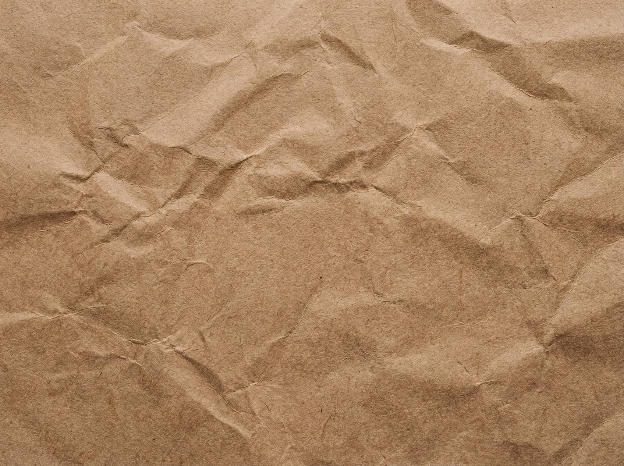A close-up, top-down view of a crumpled sheet of light brown kraft paper, showing prominent wrinkles and folds.