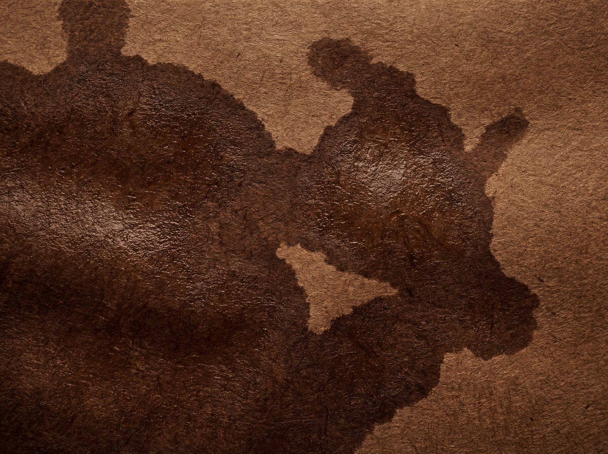 A close-up, abstract view of dark brown crumpled kraft paper with textured folds and a slightly glossy, wet-looking stain.