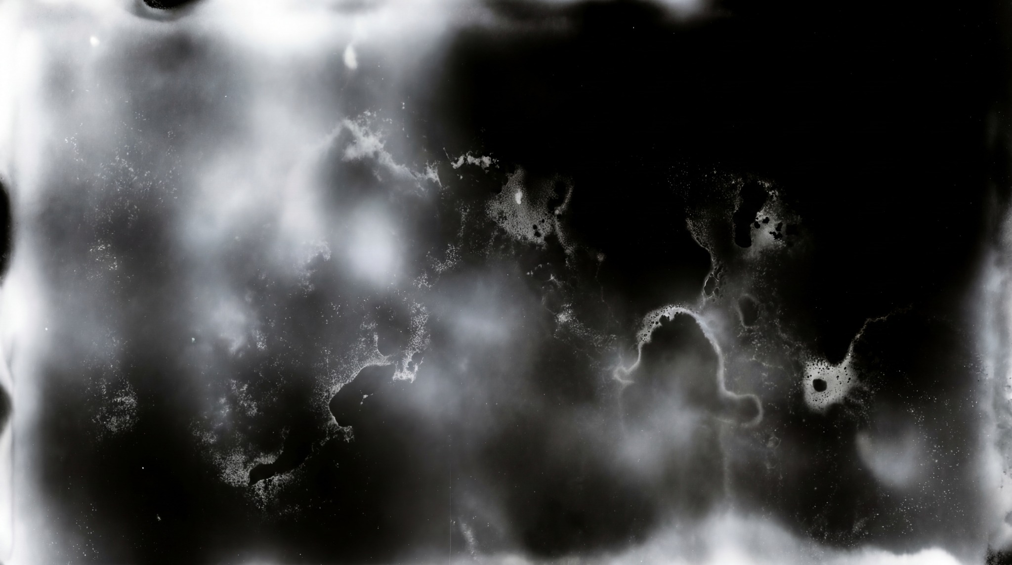 An abstract, monochrome light leak texture with swirling white and gray tones against a black background.