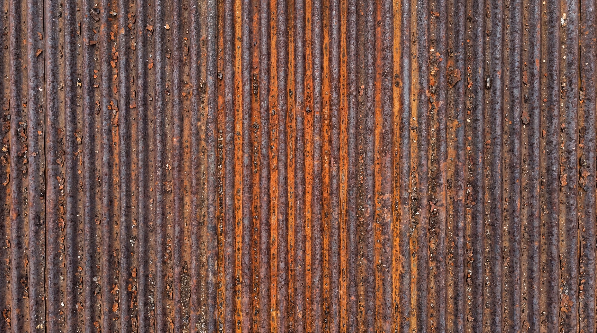 Close-up of a weathered, vertical corrugated steel sheet featuring heavy rust oxidation and orange patina.
