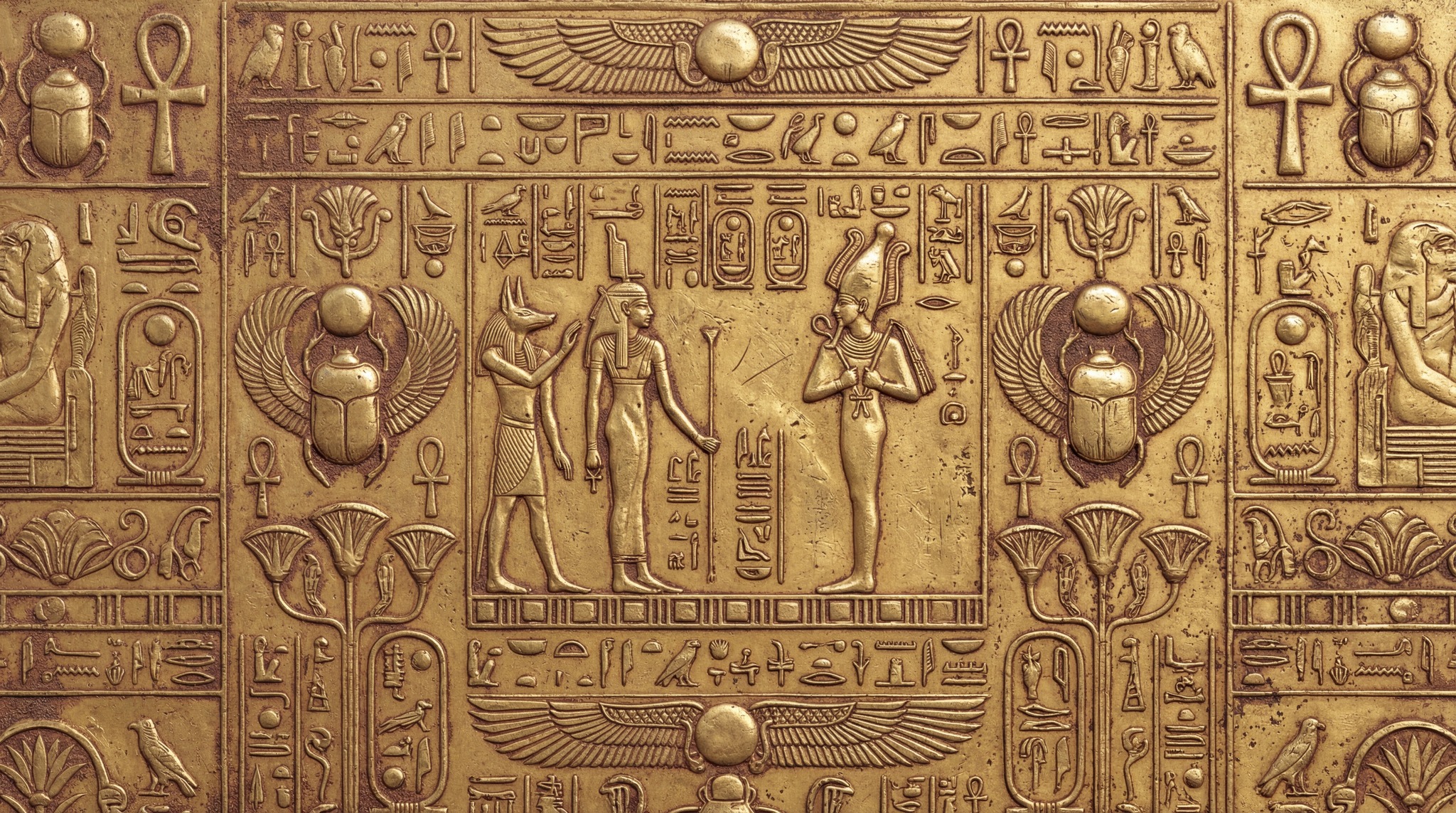 Close up of a metallic gold surface embossed with ancient Egyptian deities and hieroglyphics in a bas-relief style.