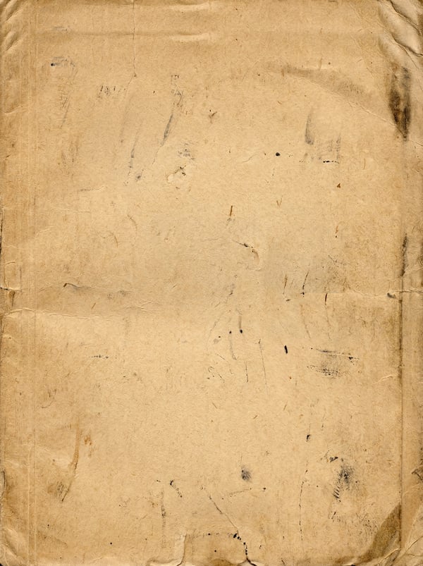 A close-up view of aged, yellowed parchment paper with visible creases, folds, and scattered dark ink splatters.
