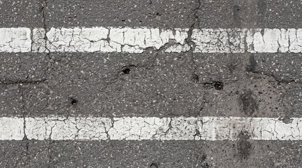 Close-up of a damaged asphalt road surface with two parallel, worn white road markings.