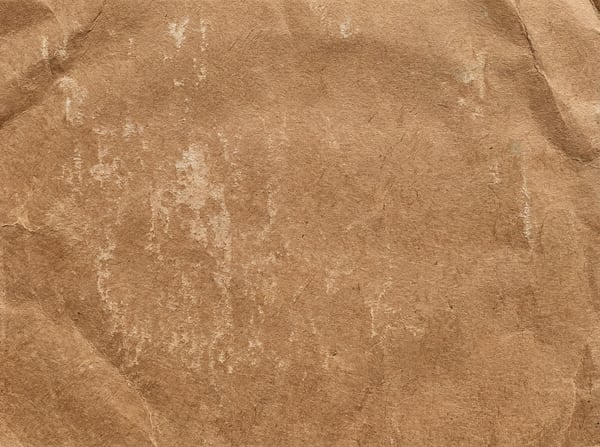 A detailed close-up texture of crumpled light brown kraft paper with visible fibers and white distressed marks.