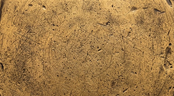 Close-up of a textured gold surface with numerous fine scratches and pitting.