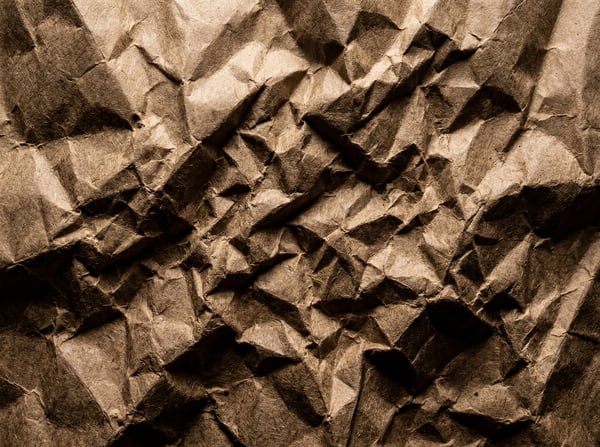A close-up, top-down view of heavily crumpled dark brown kraft paper, showing deep creases and shadows.