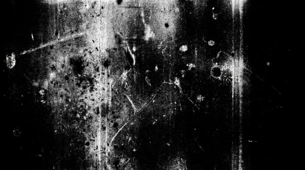 A black and white texture overlay featuring dense white dust particles, numerous scratches, and some circular blotches, resembling aged analog film.