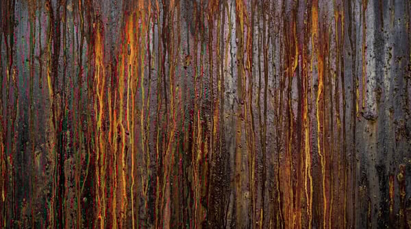 A dark, weathered metal surface with pronounced vertical streaks of orange and brown rust drips.