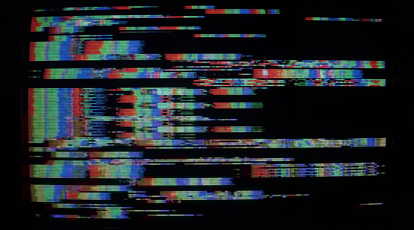 A digital screen displaying corrupted scanlines with vibrant red, green, and blue color bleeding effects against a black background.