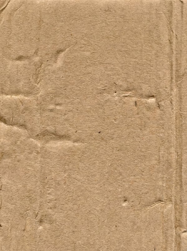 A close-up, full-frame view of a light brown, corrugated cardboard surface with visible creases and rough fibers.