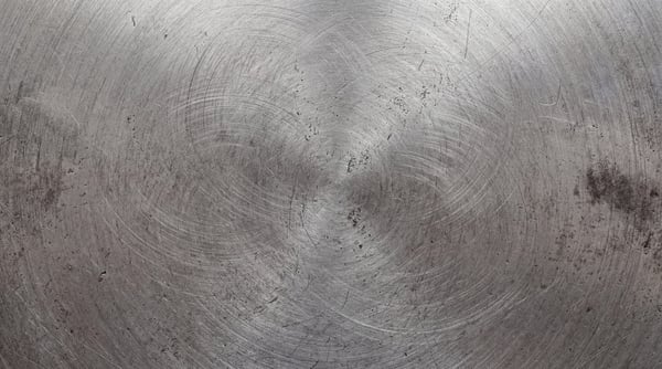 A close-up of a circular brushed steel surface with heavy rotational scratches and industrial wear.