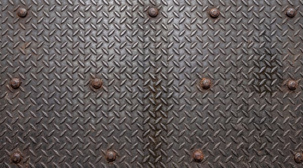 A close-up of a dark industrial diamond plate steel sheet with visible bolt heads.
