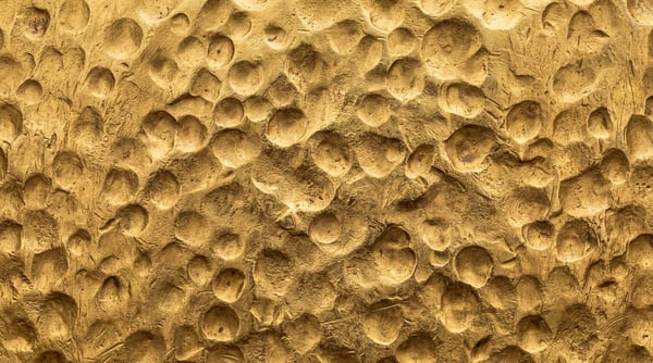 Close-up view of a golden surface with numerous irregular, circular indentations, resembling hammered or molded metal.
