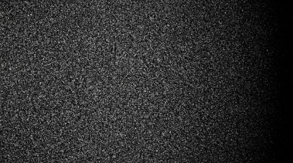 A dense, monochromatic film grain texture with subtle light falloff on the right.