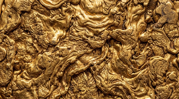 Close-up of a highly textured, molten gold surface with intricate swirling patterns and solidified liquid formations.
