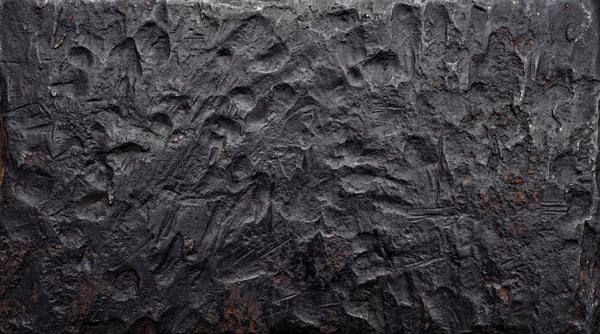 A close-up of a raw forged steel surface featuring deep impact marks, heavy indentations, and coarse dark grey metal pitting.