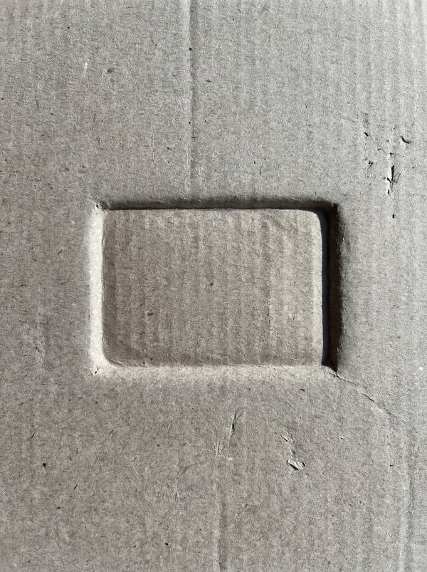 Grey cardboard texture with a prominent embossed rectangular shape in the center.