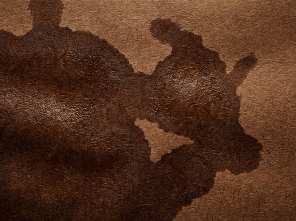 A close-up, abstract view of dark brown crumpled kraft paper with textured folds and a slightly glossy, wet-looking stain.