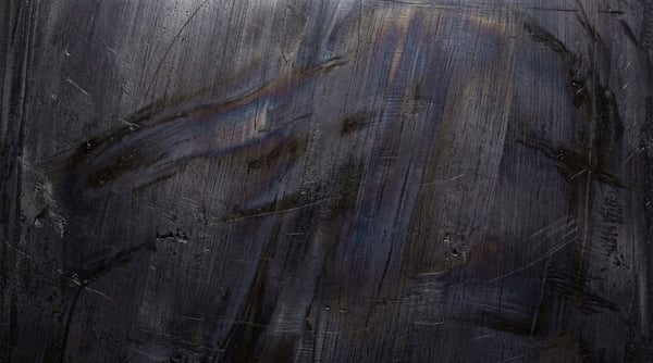 Close-up of a dark, industrial steel surface featuring heavy brush strokes, fine linear scratches, and deep metallic charcoal tones.