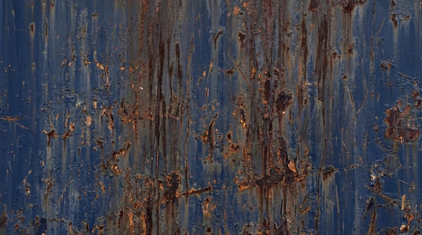 A close-up view of navy blue painted steel featuring heavy rust streaks, paint peeling, and scattered surface scratches.