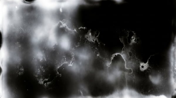 An abstract, monochrome light leak texture with swirling white and gray tones against a black background.