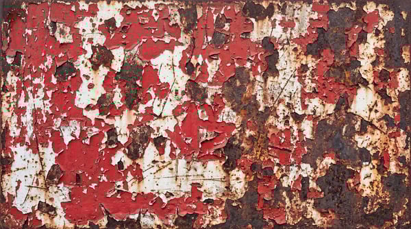 Close-up of weathered steel surface featuring layers of peeling red paint, heavy rust, and deep metallic oxidation.