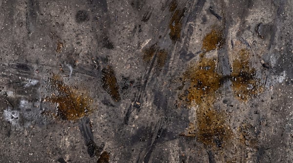 Close-up of a damaged concrete floor texture with dark oil spills and tire marks.