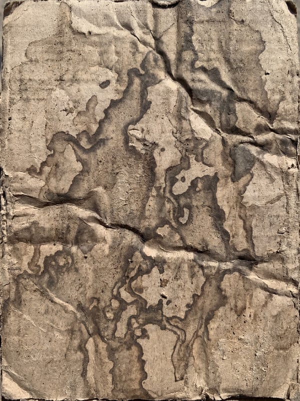 Close-up of rippled brown cardboard with dark, abstract water stains.