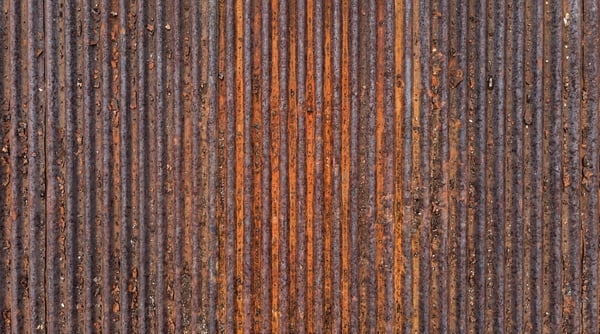 Close-up of a weathered, vertical corrugated steel sheet featuring heavy rust oxidation and orange patina.