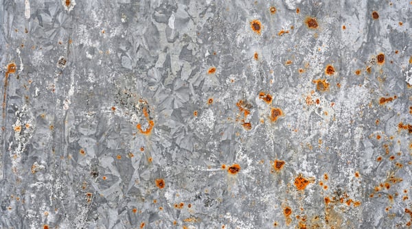 Close-up of galvanized steel with scattered, pitted orange rust.