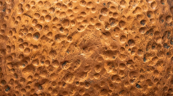 Close-up of a rustic hammered copper metal sheet with visible circular indentations and natural surface weathering.