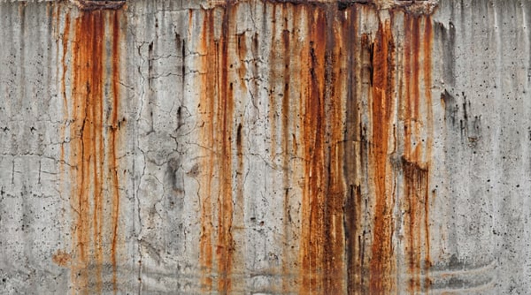 A textured concrete surface with prominent vertical streaks of rust stains running down.