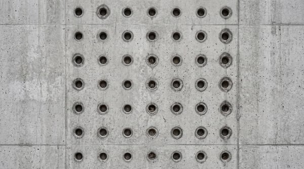 A seamless 4K texture of raw brutalist concrete with a grid of circular indentations.