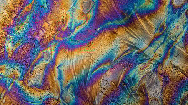 Close-up view of heat-treated steel showing vibrant iridescent temper colors with blue, purple, and gold swirling patterns.